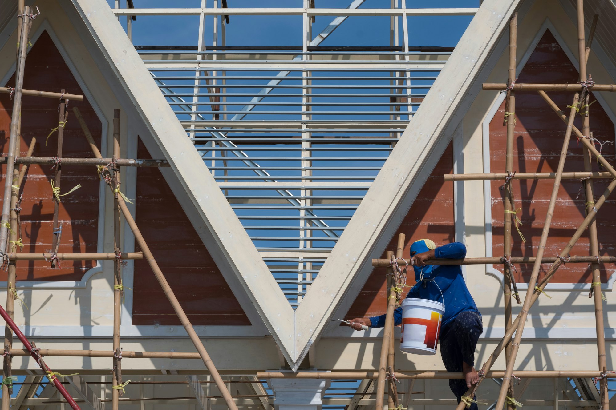 Asian builder worker on wooden scaffold is painting gable roof of vintage house structure
